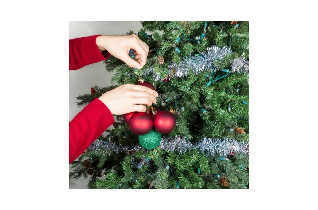 Two hands removing green and red ornaments from a tree