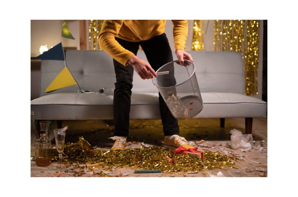 Man in a yellow sweater bent over and picking up party confetti and gift boxes from the floor